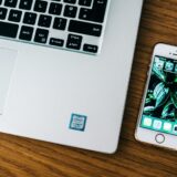 Laptop deschis și telefon mobil pe un birou, ambele afișând ecrane cu pictograme de aplicații