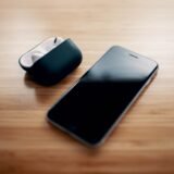 Telefon mobil conectat la încărcător, așezat pe o noptieră lângă o veioză aprinsă