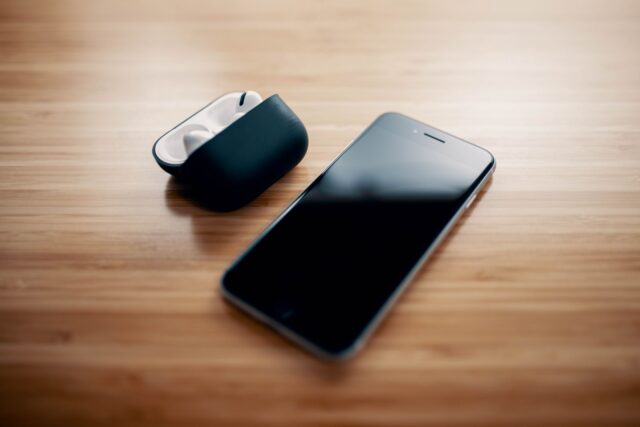 Telefon mobil conectat la încărcător, așezat pe o noptieră lângă o veioză aprinsă