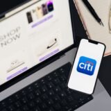 Telefon ținut în mână, cu aplicația bancară deschisă pe ecran, deasupra unui card de plată așezat pe masă