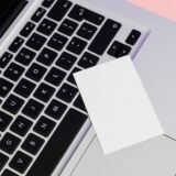 Tastatură de laptop curățată cu o pensulă moale, lângă o lavetă din microfibră și o șurubelniță mică