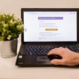 Mâini pe tastatura unui laptop, cu un e-mail deschis pe ecran, analizat cu atenție înainte de a da clic