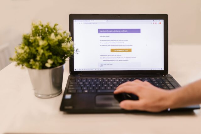 Mâini pe tastatura unui laptop, cu un e-mail deschis pe ecran, analizat cu atenție înainte de a da clic
